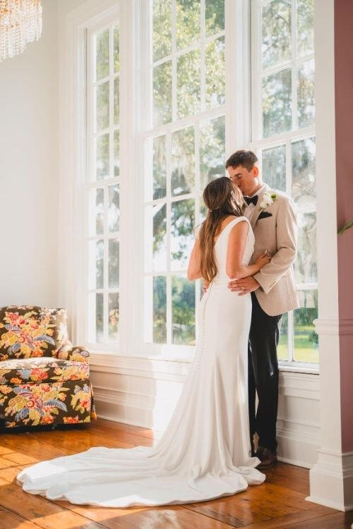 A couple kisses on their wedding day beside a large window in a historic Greenville home.